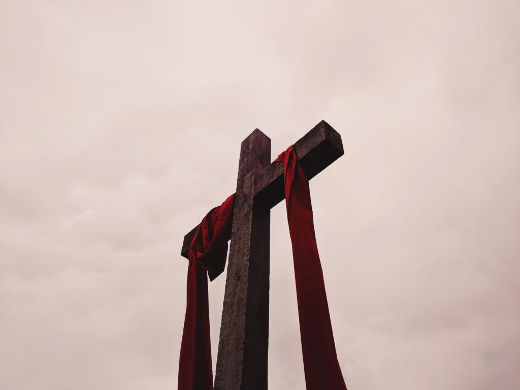 Cross with red cloth against cloudy sky.